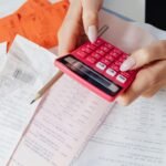 Hands using a red calculator surrounded by financial documents and receipts, symbolizing financial management.