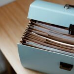 From above of opened modern briefcase with prepared papers placed on timber table in soft focus